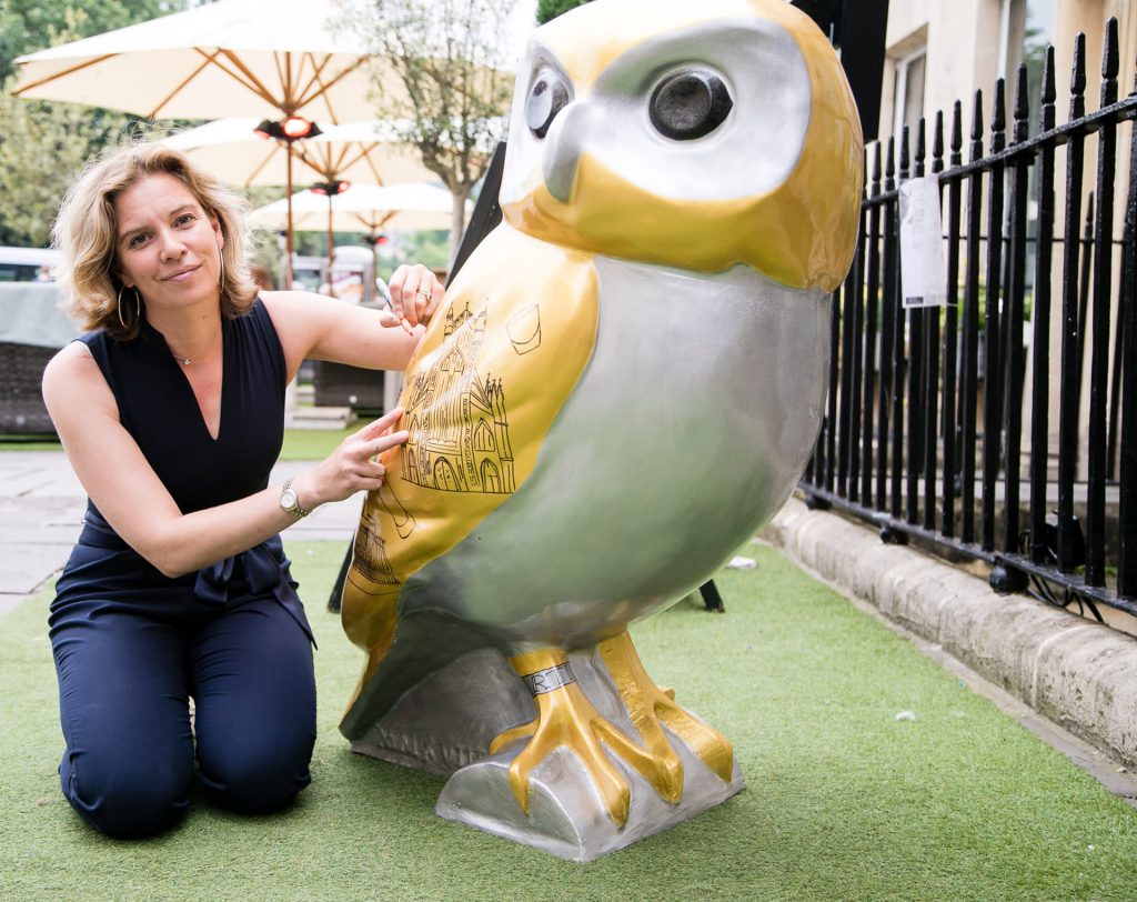 Emma Taylor outside The Abbey Hotel signing her painted artwork owl, Artis